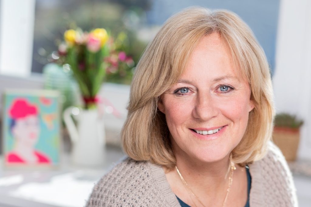 Über mich: Petra Radermacher vor einem Tisch mit einem Blumenstrauß und Bild